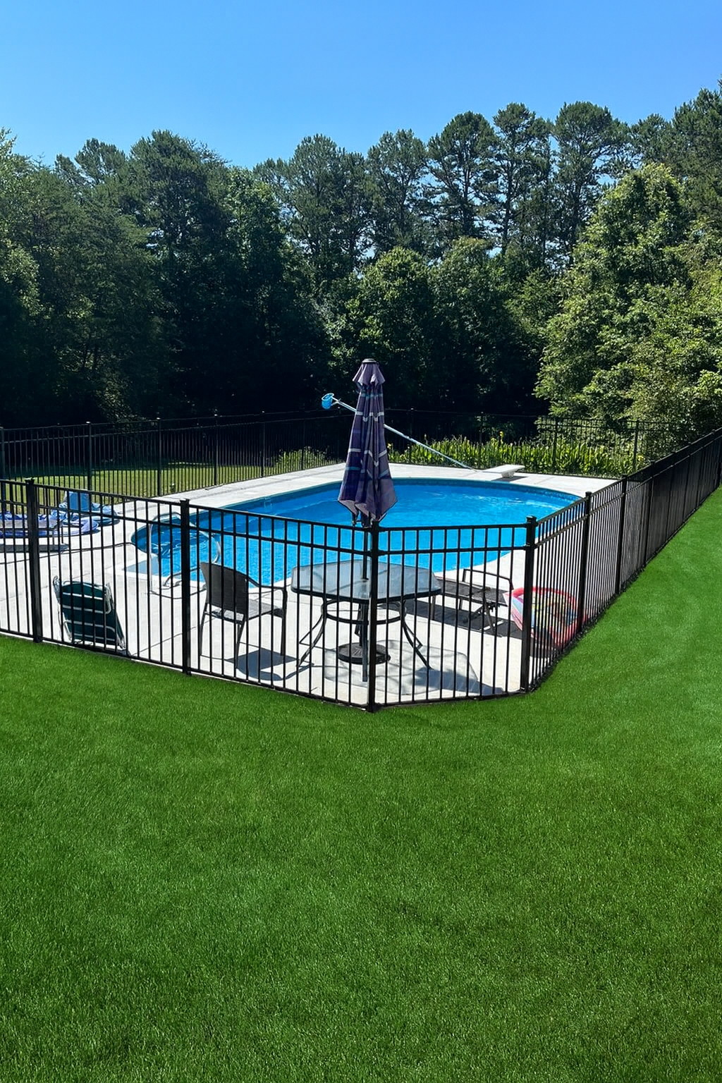 Stone pillars with ornate black iron gate and lampposts, driveway, and distant houses under a cloudy sky.