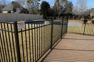 Black metal fence surrounding a wooden deck and a grassy yard. 