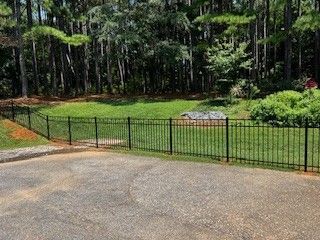 Black metal fence bordering a grassy area with trees in the background, set on a concrete surface.