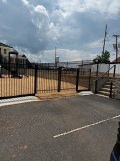 Black gated playground with stairs and a small play structure against a cloudy sky.