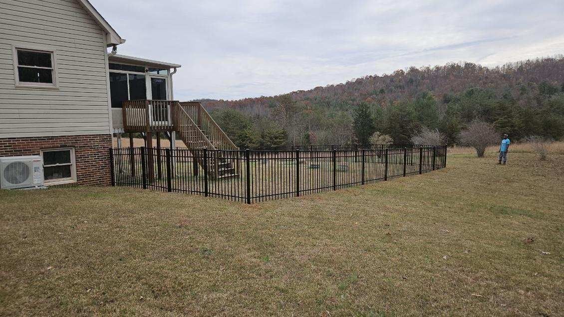 House with deck, surrounded by a worn fence, with a person standing in a grassy field. Overcast day.