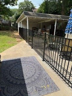 Black metal fence bordering a concrete patio with an outdoor rug and covered patio area in the background.