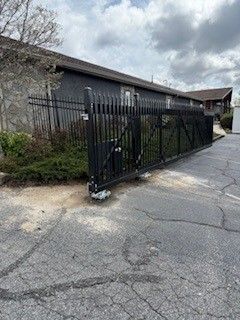 Black security gate, open, blocking access to a building and parking area.