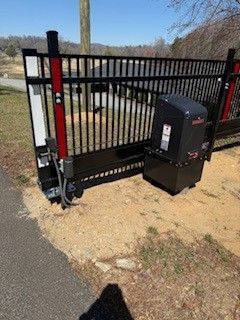 Black metal sliding gate with an automatic opener, located outdoors next to a driveway and grassy area.