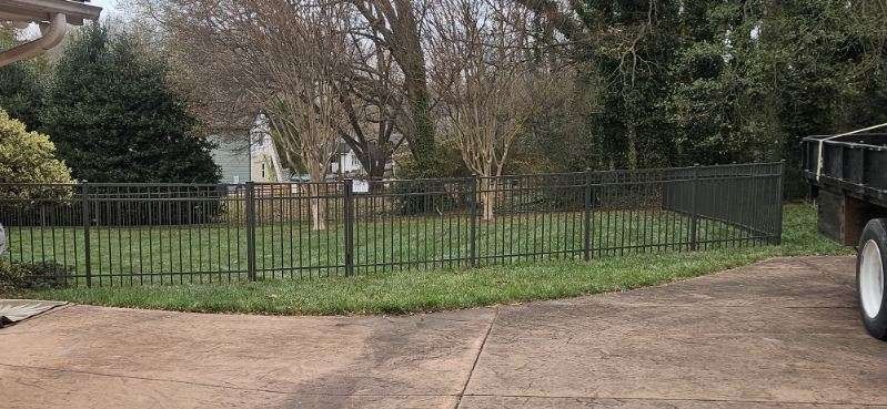Black iron fence surrounding grassy area, house in background, truck on the right.