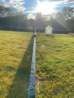 Green field with a black fence, greenhouse in the background, sun shining.