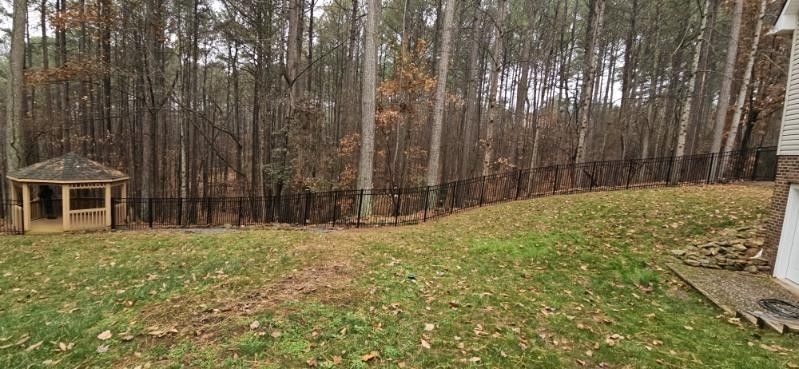 A gazebo and a fence in a backyard with a forest background. Fallen leaves on the grass.