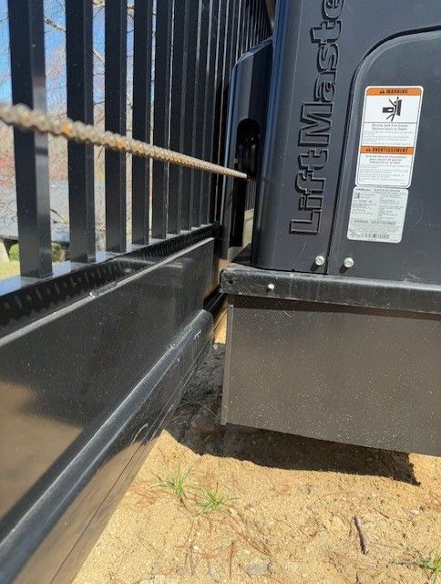 Black gate and LiftMaster motor, with chain attached, on a sandy surface.