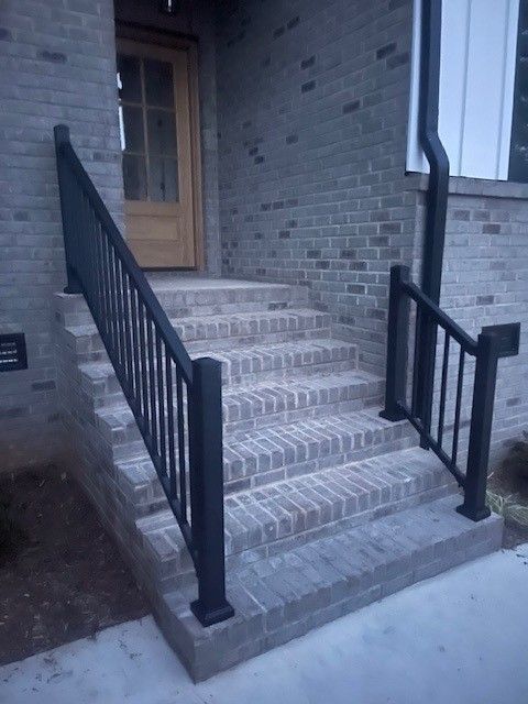 Brick steps leading up to a wooden door, black handrails on either side.