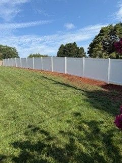 White vinyl fence borders a green lawn under a bright blue sky.