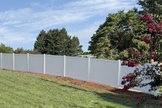 White vinyl fence in a grassy yard, with trees and blue sky visible.