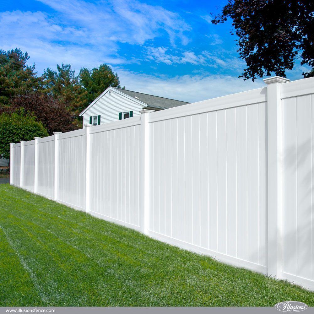 White vinyl fence surrounding a green lawn in front of a house under a blue sky.