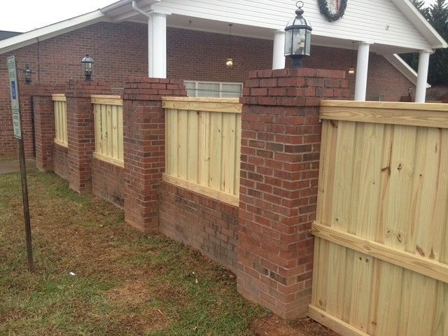 Brick and wood fence outside a building with lampposts atop brick pillars.