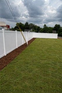 White fence bordering a lawn, mulch bed along the base. Power lines overhead against a cloudy sky.