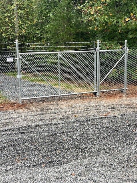 Chain link fence gate blocking a gravel road in front of trees.