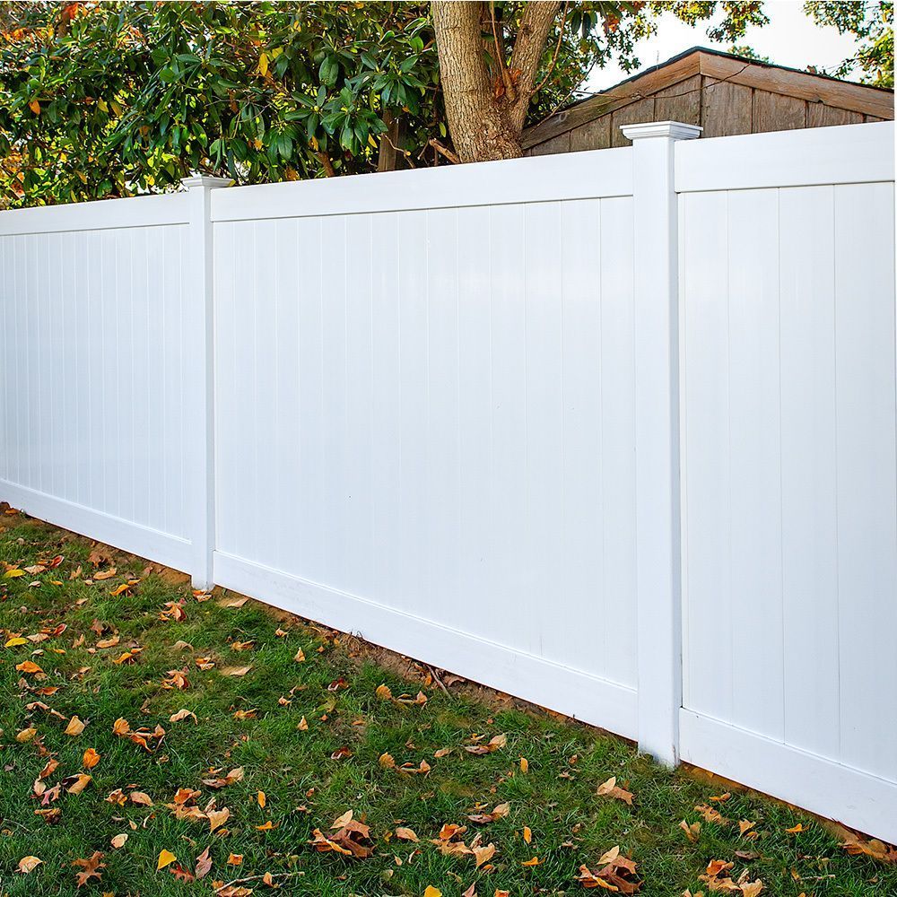 White vinyl fence in a yard with grass and fallen leaves. A tree and shed are in the background.