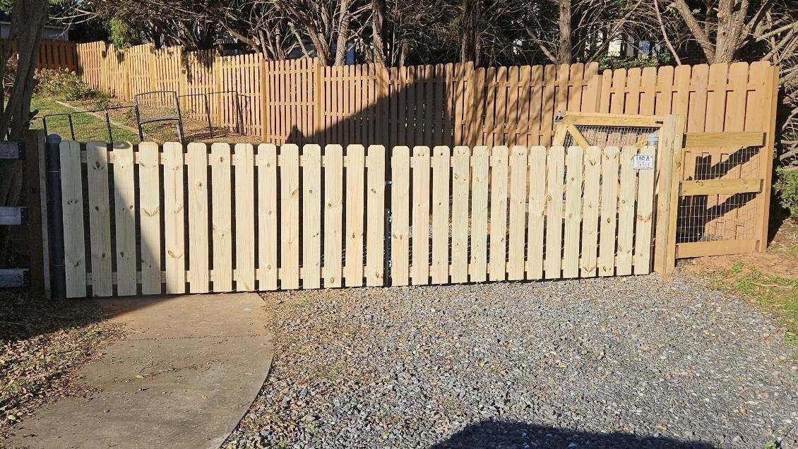 Wooden fence with two gate doors open on gravel driveway.