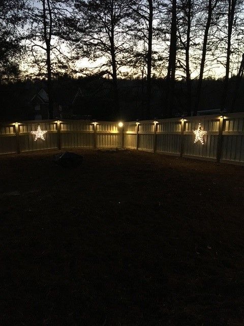 A fence with lights and star decorations at dusk.