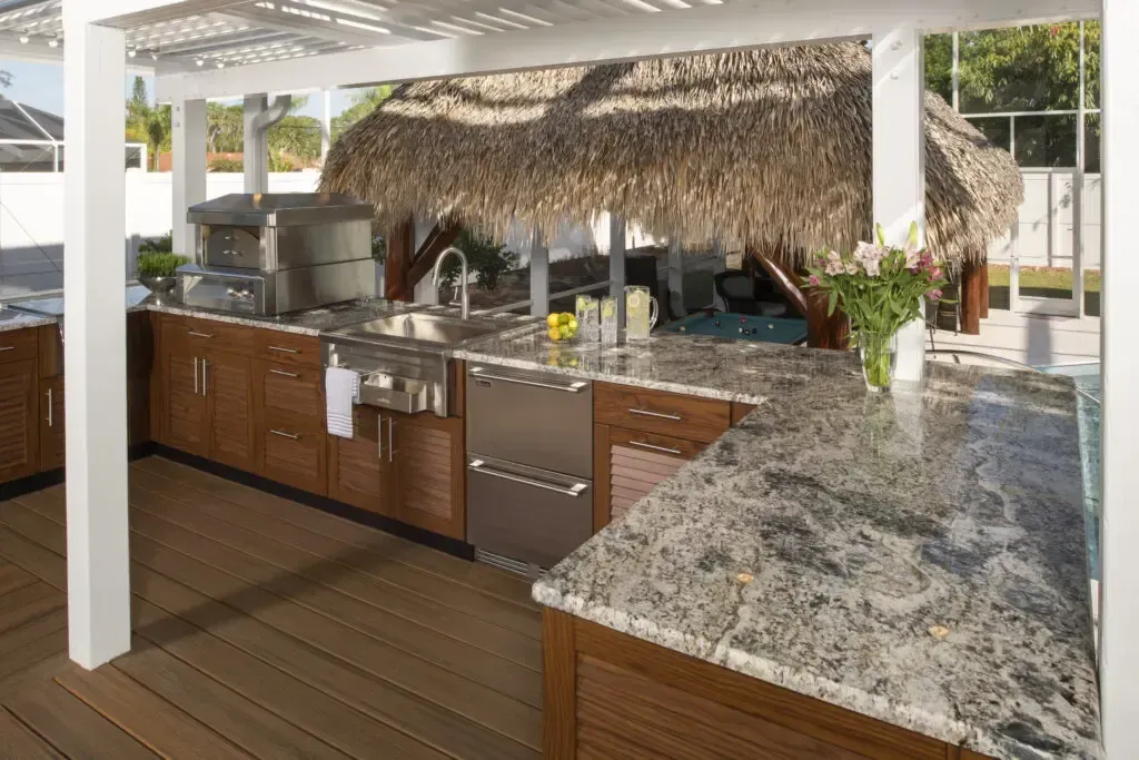 Outdoor kitchen with granite countertops, stainless steel appliances, and a thatched roof.