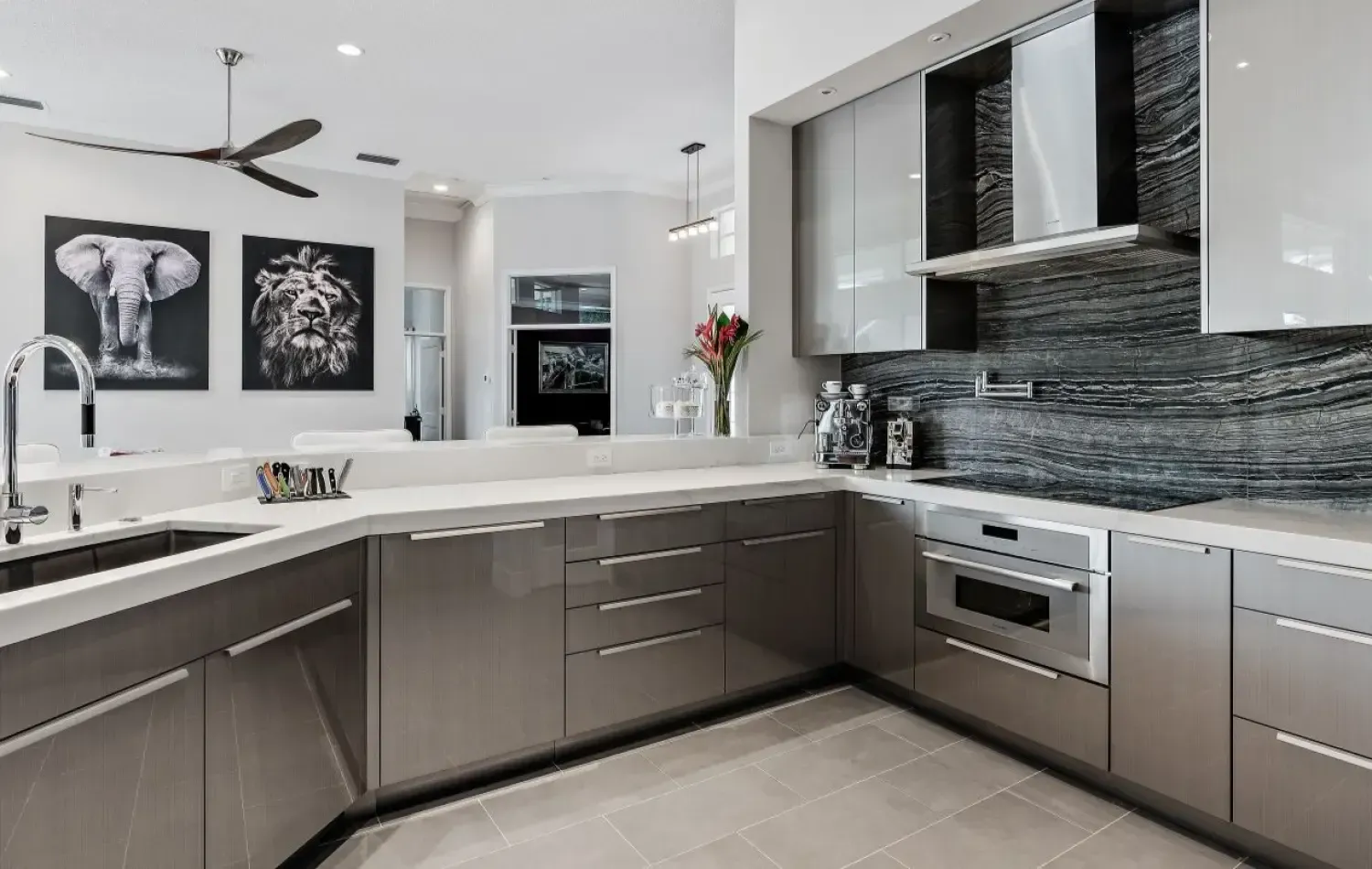 Modern kitchen with gray cabinets, marble countertops, stainless steel appliances, and animal artwork.