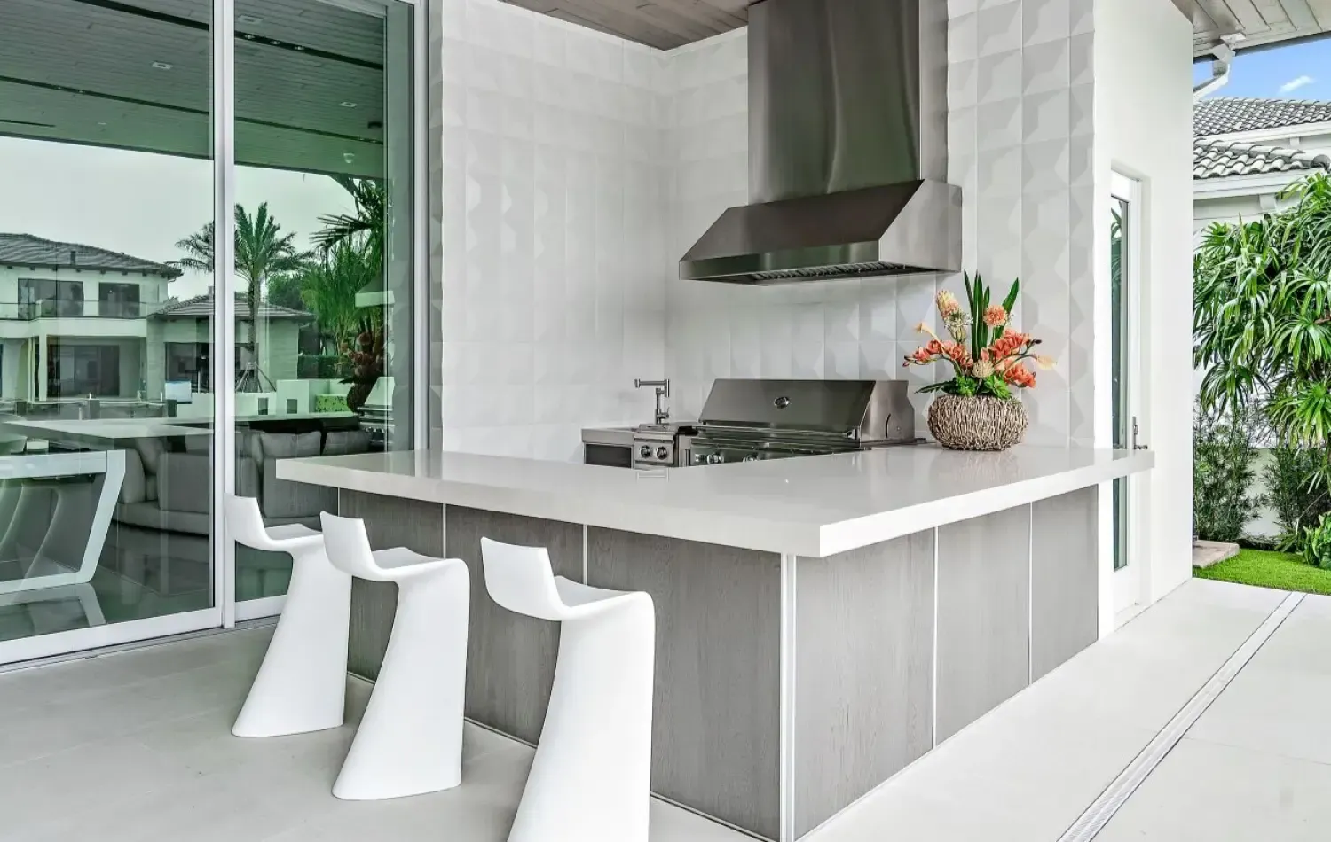 Outdoor kitchen with white countertops, stainless steel appliances, and white bar stools.
