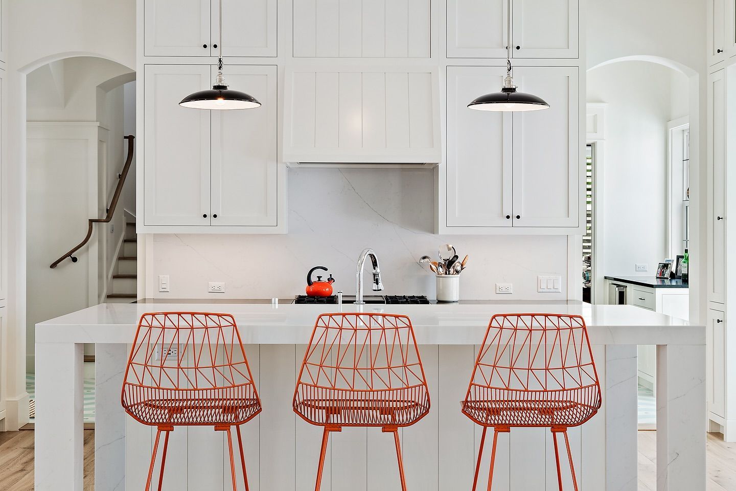 Kitchen with white cabinets, island and orange wire bar stools. Two pendant lights hang overhead.