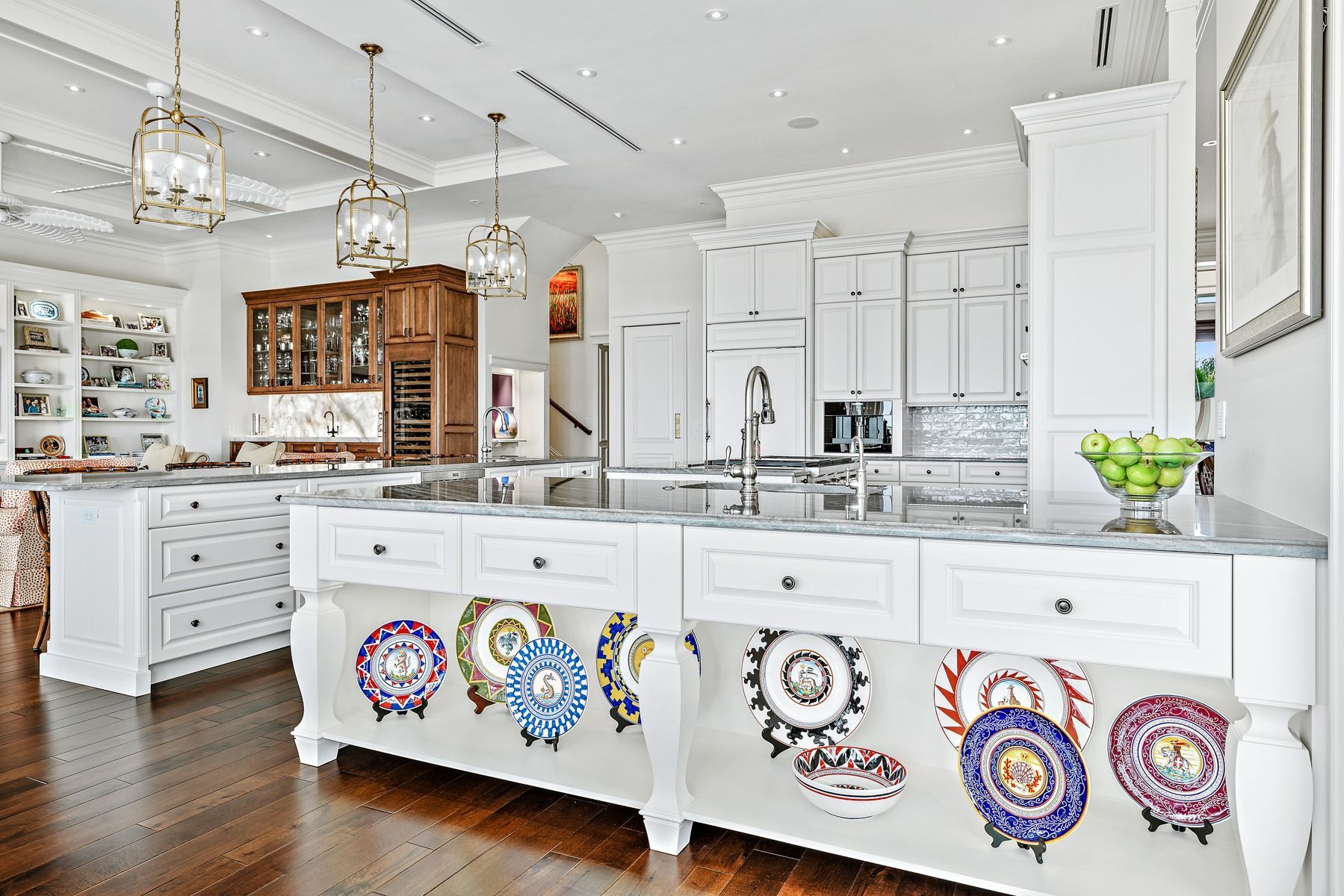 Spacious, white kitchen with two islands, dark wood floors, and hanging decorative plates.