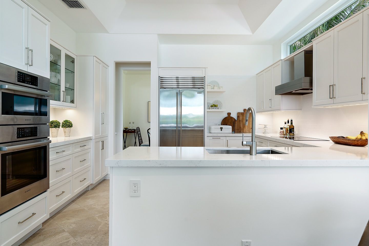 Bright white modern kitchen with stainless steel appliances, a large island, and a view of the outdoors.