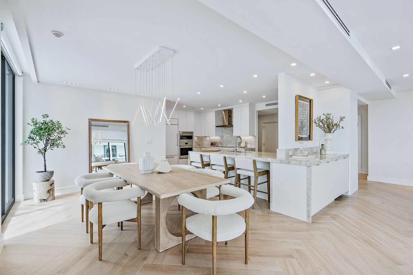 Bright, modern open-concept kitchen and dining area with white walls, light wood floors, and fluffy white chairs around a long table.