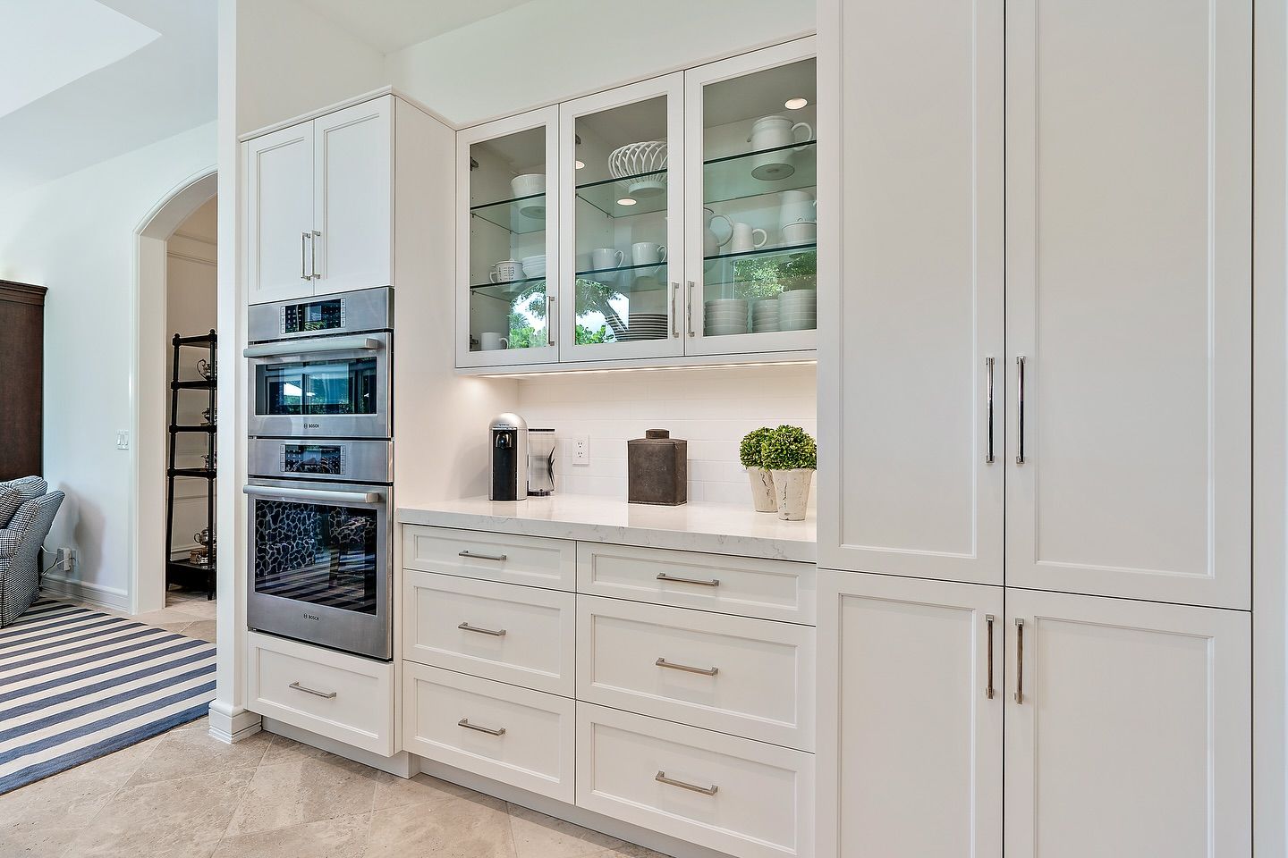 White kitchen cabinets with built-in ovens, glass-front display, and drawers.