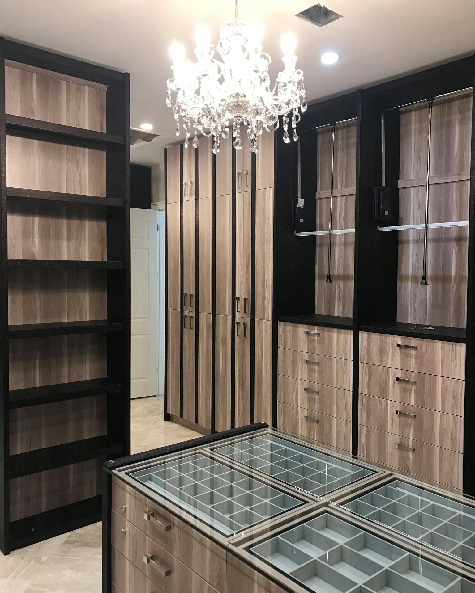 Walk-in closet with built-in shelving, drawers, and a central island with glass top; chandelier overhead.