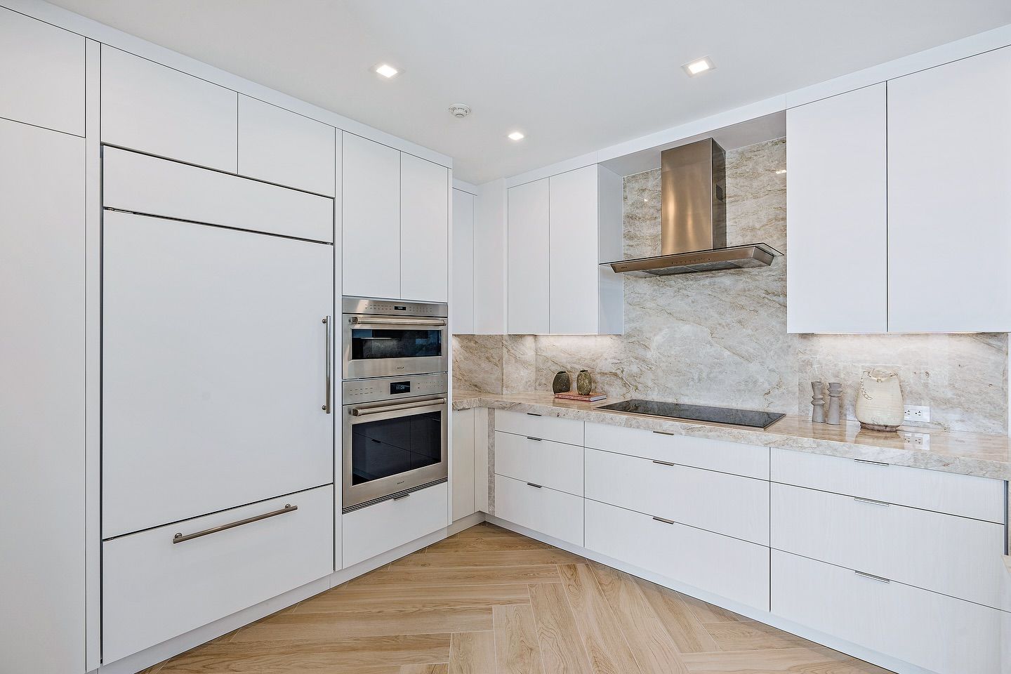 White modern kitchen with light wood floors, stainless steel appliances, and marble backsplash.
