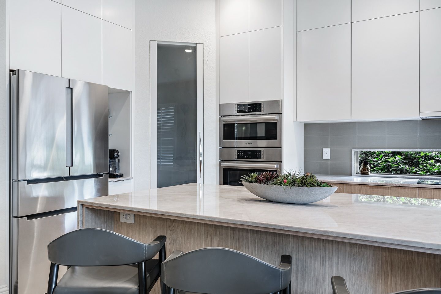 Modern white kitchen with stainless steel appliances, light wood accents, and a marble countertop.