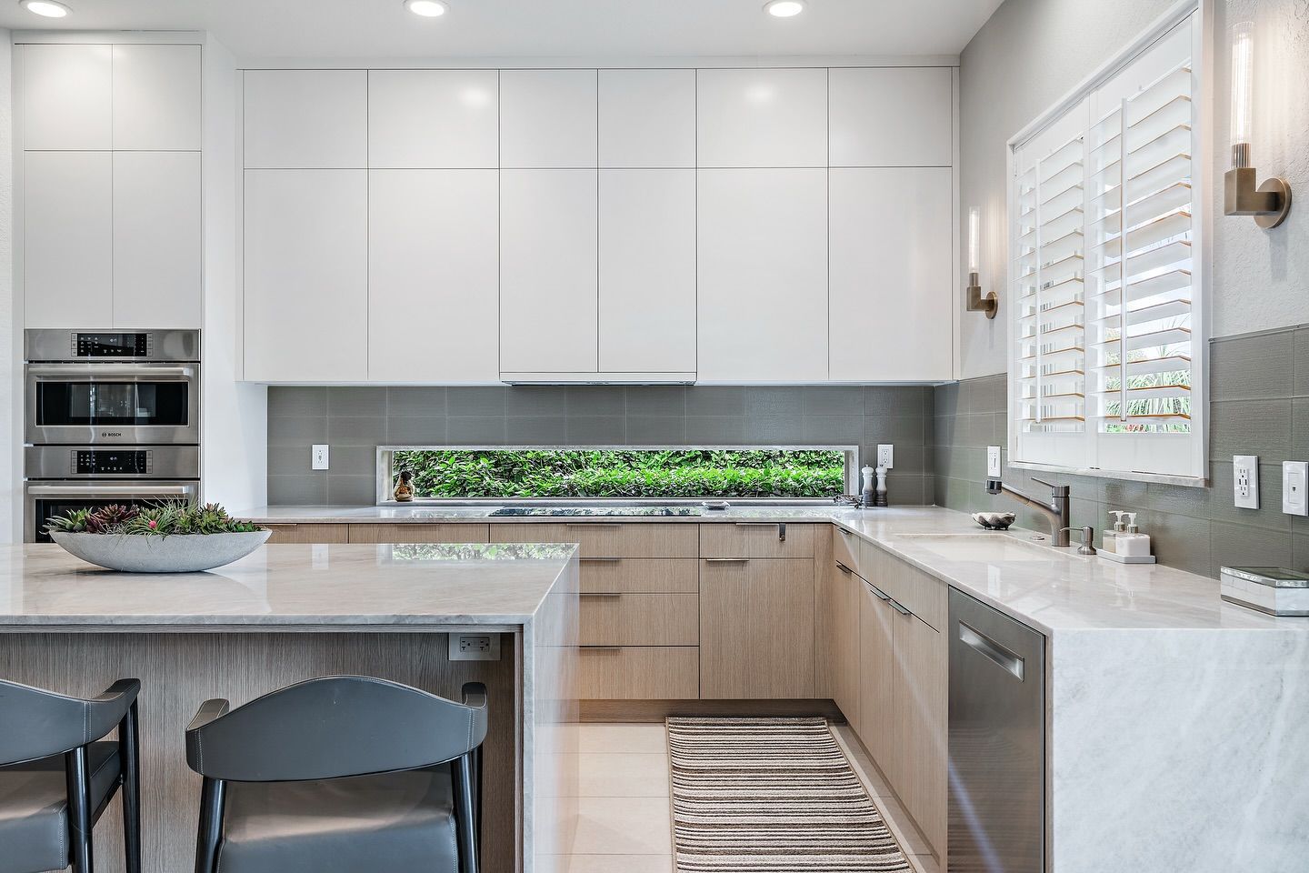 Modern kitchen with white upper cabinets, light wood lowers, gray backsplash, and island.