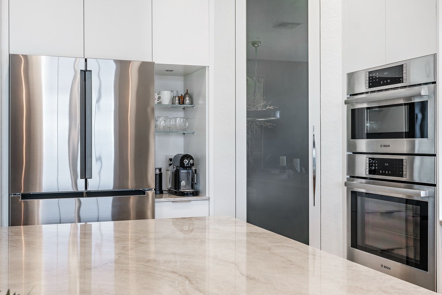 Modern kitchen with stainless steel appliances, marble countertops, and built-in ovens.