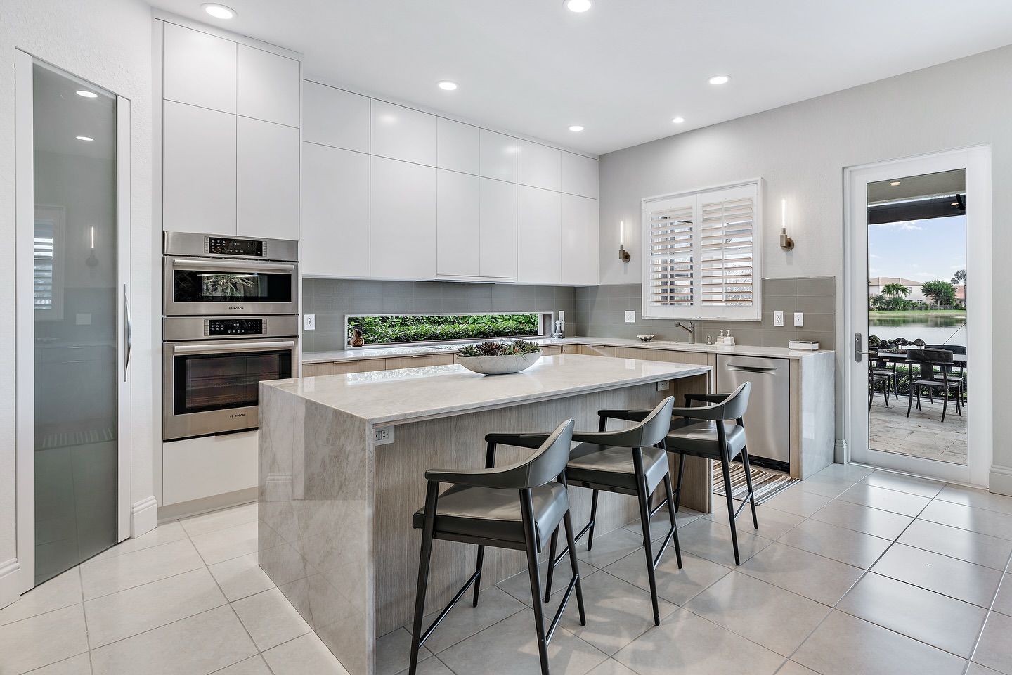 Modern kitchen with white cabinets, island with stools, and outdoor view.