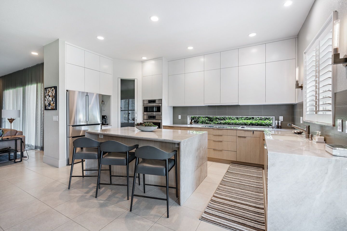 Modern kitchen with white cabinets, large island with seating, stainless steel appliances, and wood and grey accents.