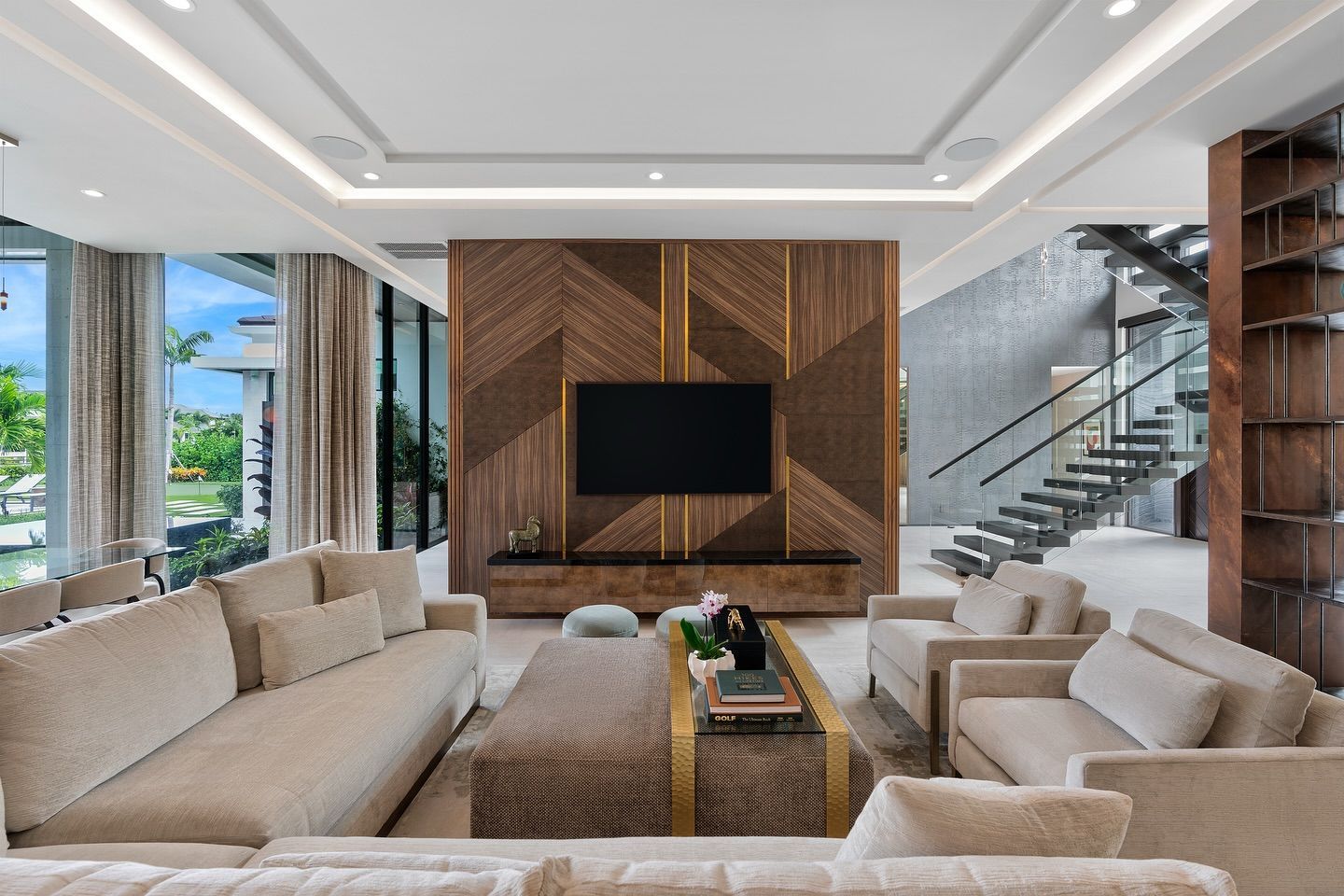 Luxury living room with beige furniture, large TV, and geometric wood paneling.
