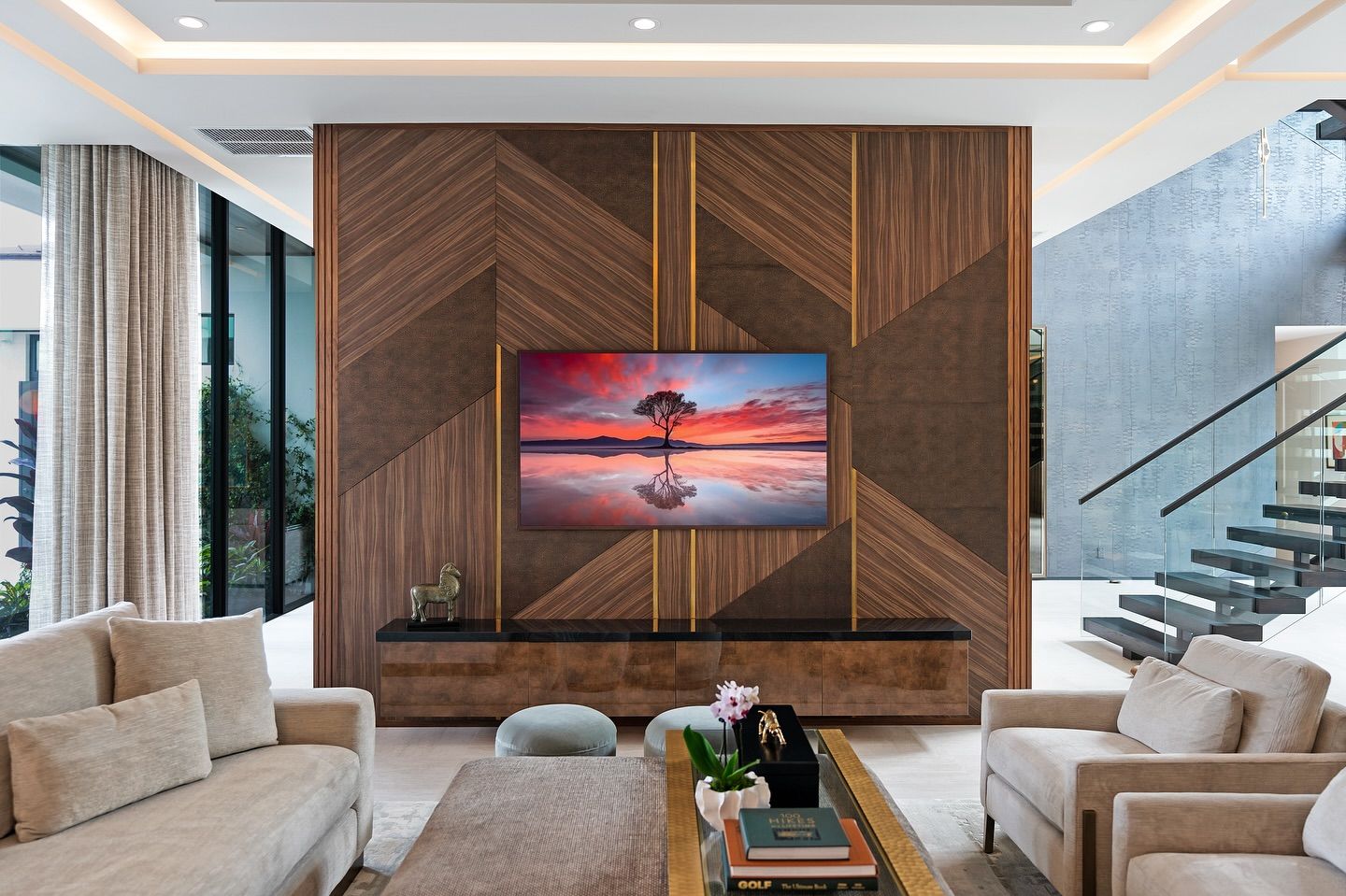 Living room with a large TV on a wood panel wall with gold accents, facing two beige sofas.