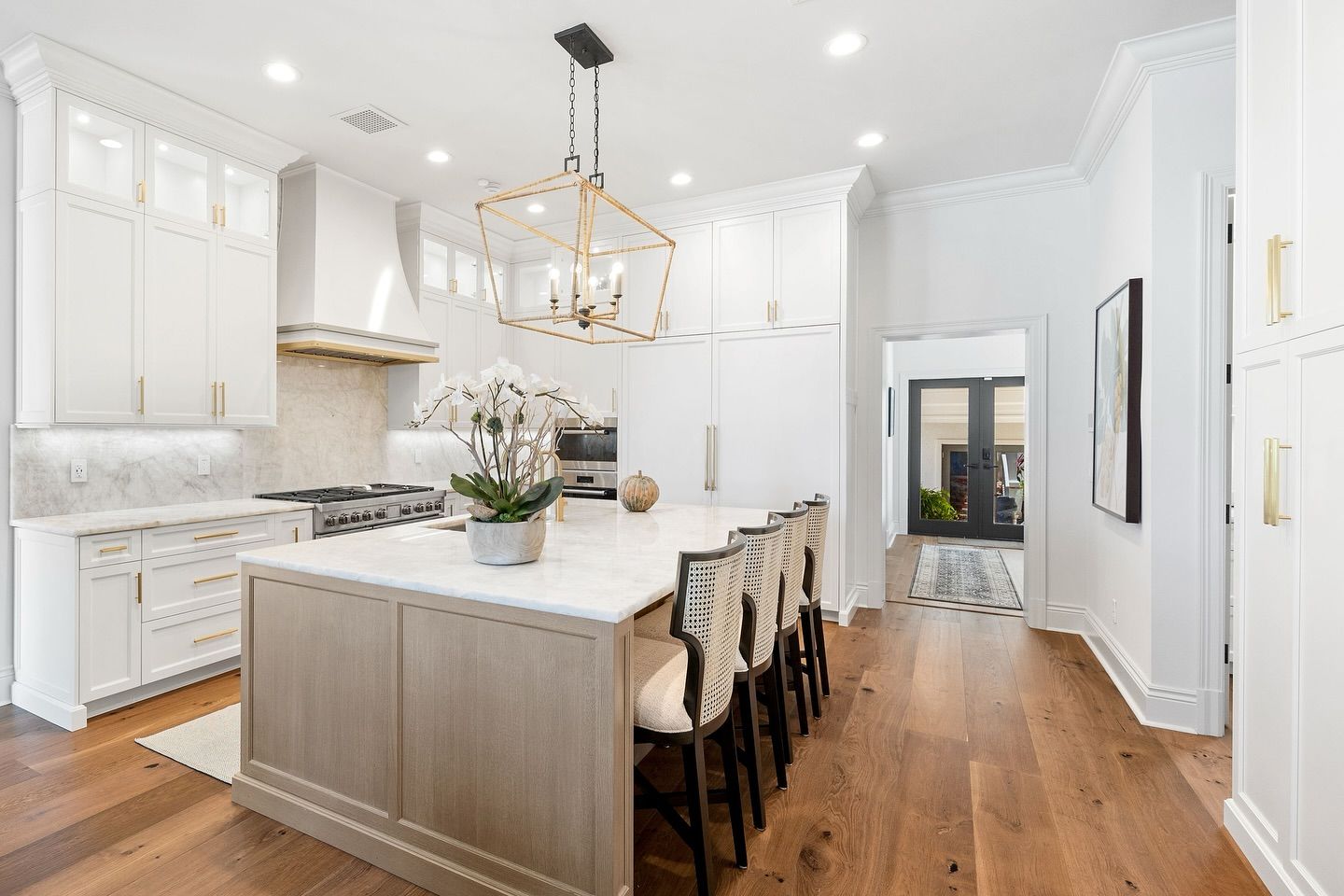 Bright kitchen with island and light wood floor. White cabinets, marble countertops, gold chandelier.