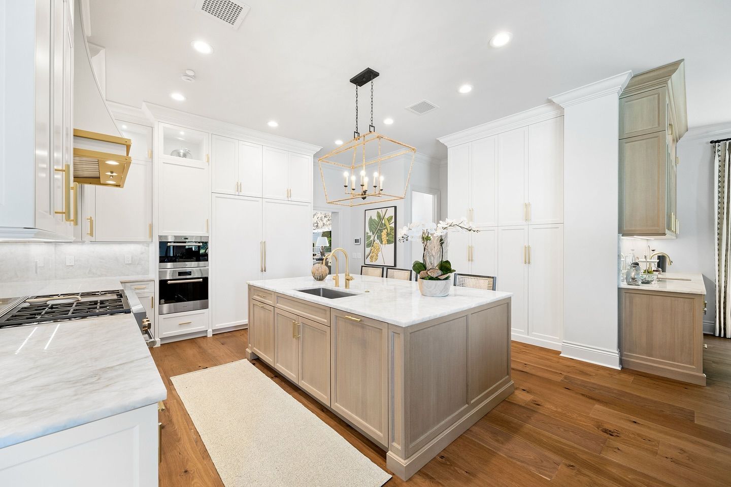 Bright kitchen with a large island, white cabinets, and wood flooring.