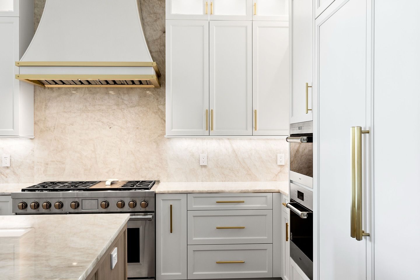 White kitchen with gold accents; range, cabinets, oven, and vent hood are visible.