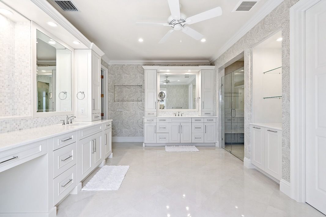 Bright white bathroom with double vanity, central vanity, shower, and ceiling fan.