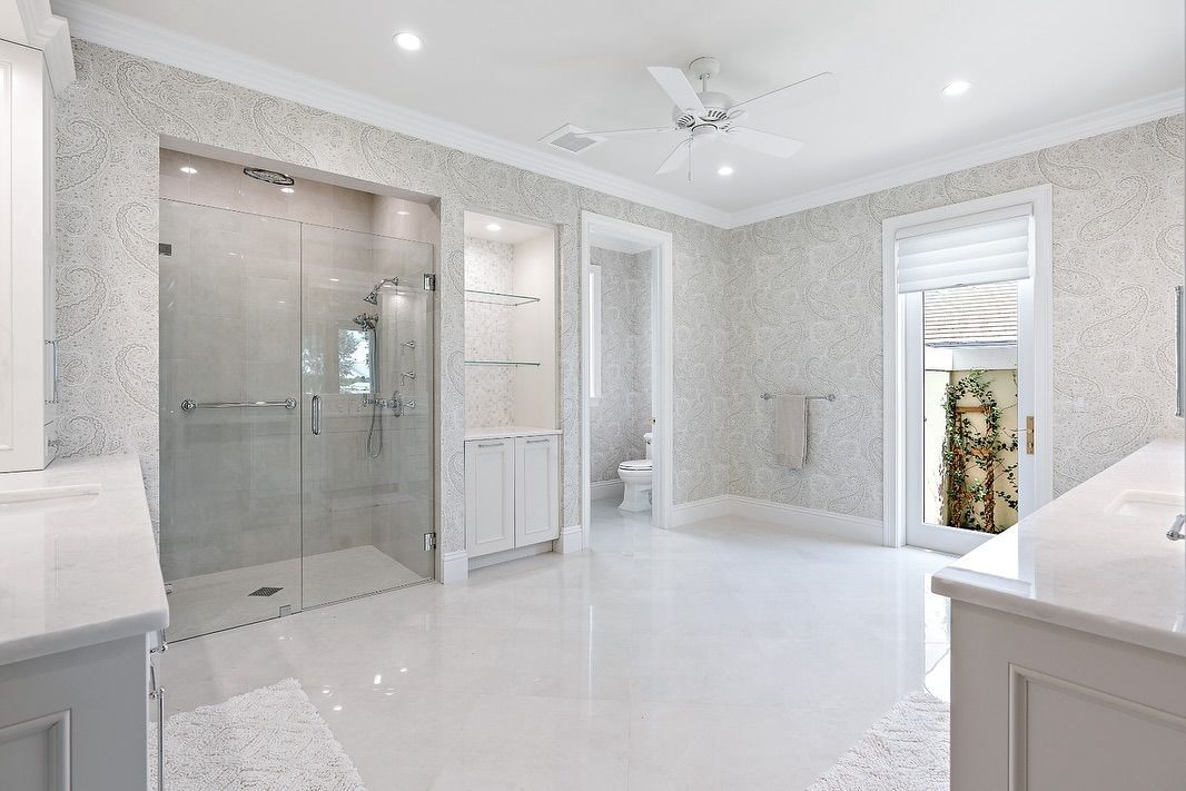 Spacious white bathroom with a glass shower, textured walls, and a door to an outdoor space.