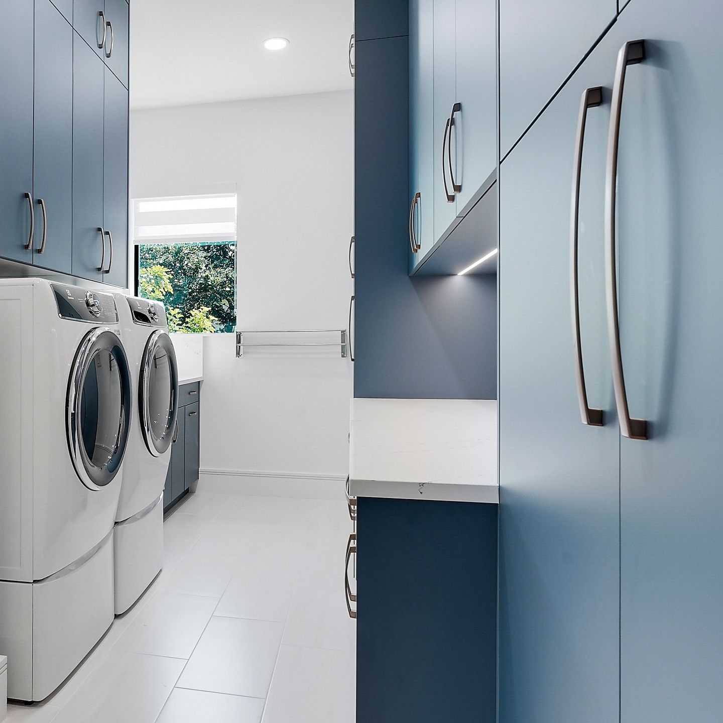 Blue laundry room with a washer and dryer, cabinets, and a window.