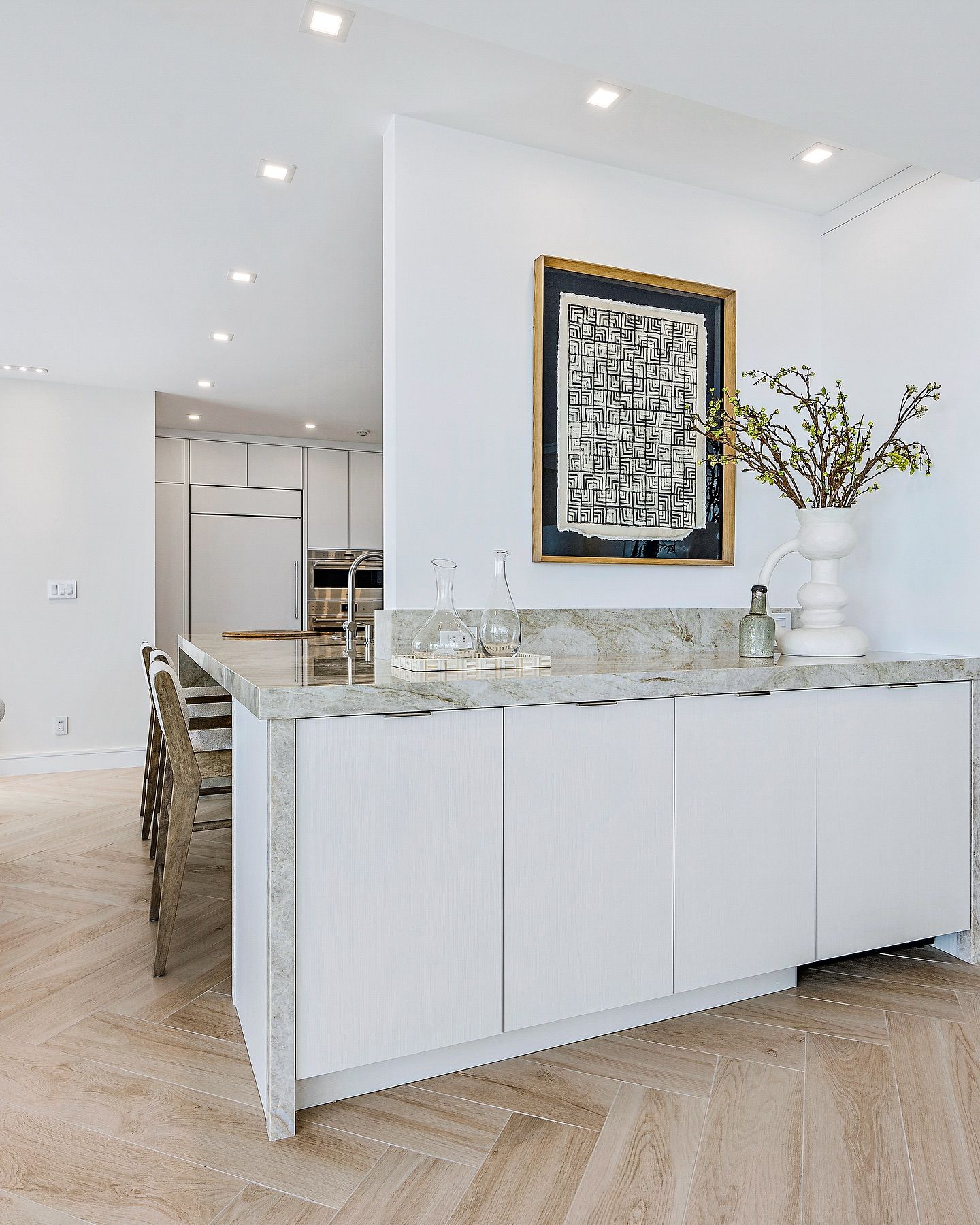White kitchen island with granite countertop, white cabinets, artwork, vase of flowers.