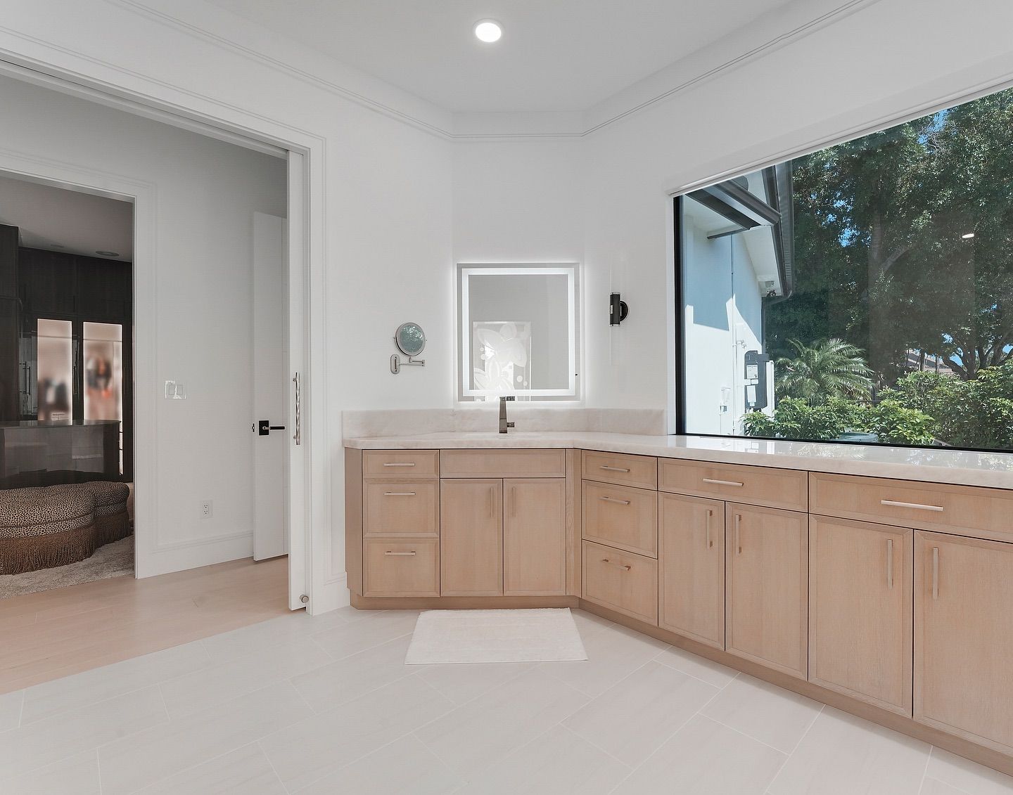 Bathroom with light wood cabinets, large window overlooking trees, and a doorway.
