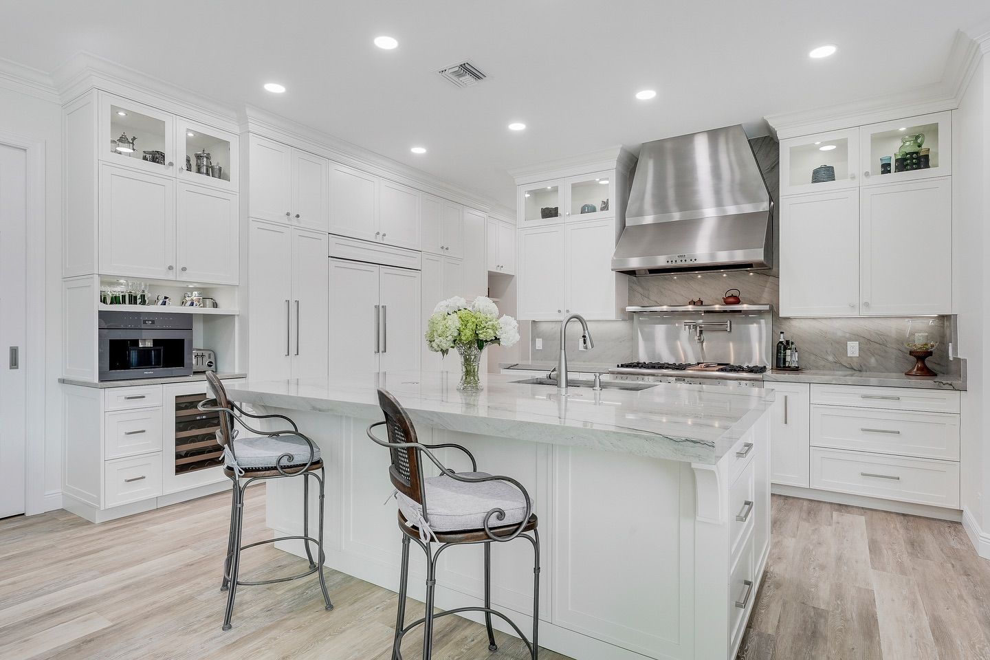 White kitchen with island, stainless steel range hood, and bar stools.