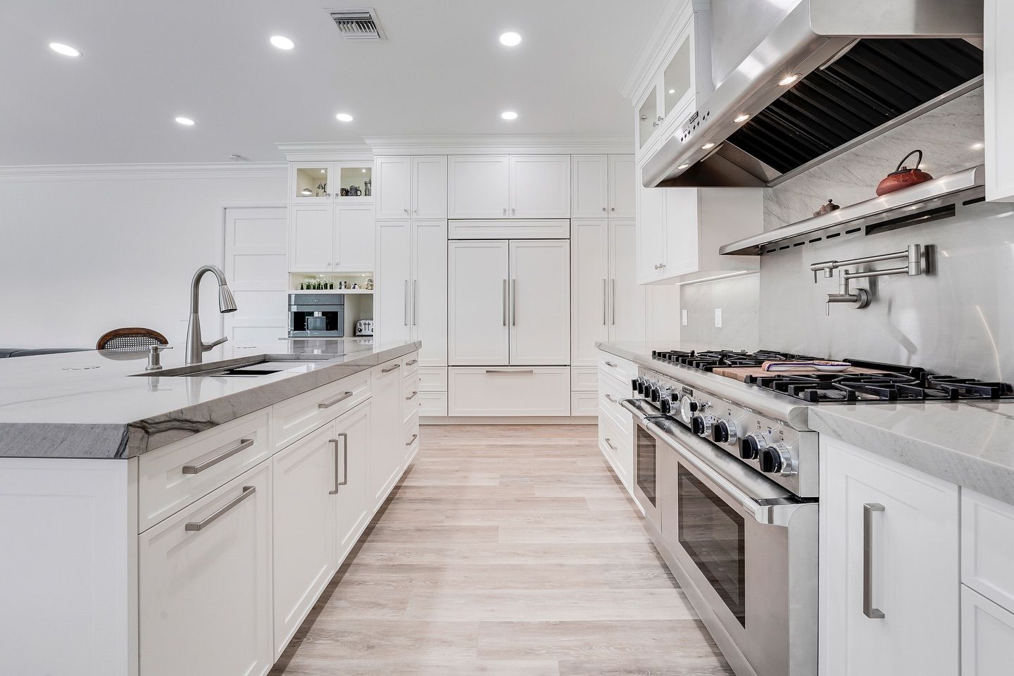 White kitchen with island, stainless steel appliances, and marble countertops.