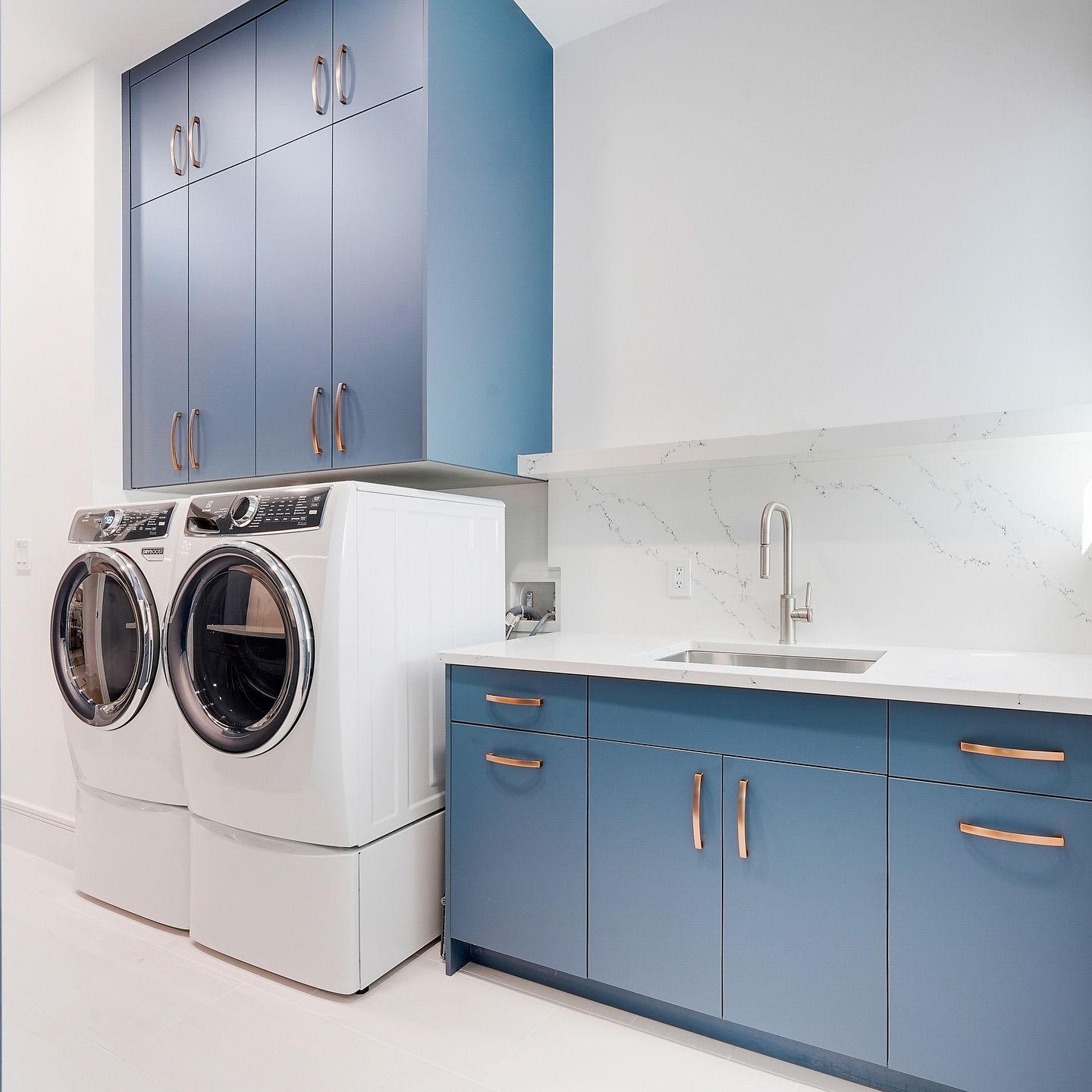 Laundry room with blue cabinets, white appliances, and sink.